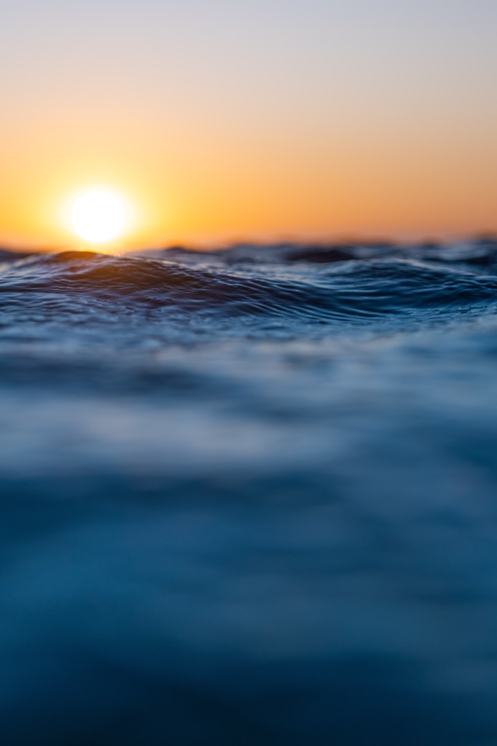 Klarheit gewinnen. Sonnenuntergang über ruhigem Wasser mit sanften Wellen und orangefarbener Helligkeit.